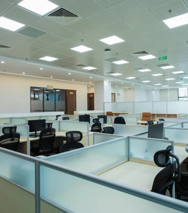 Bright, spacious modern open-plan office with rows of partitioned workstations, ergonomic office chairs, desks, and overhead fluorescent lighting.