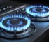 Close-up of a modern gas cooktop with two burners lit, showing bright blue flames on a sleek black surface.