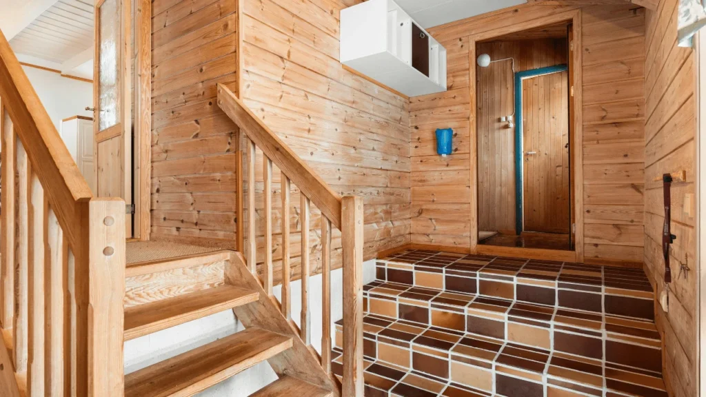 Wooden staircase and tiled steps leading through the interior of a cozy wood-paneled home, with a wooden door and railing visible.